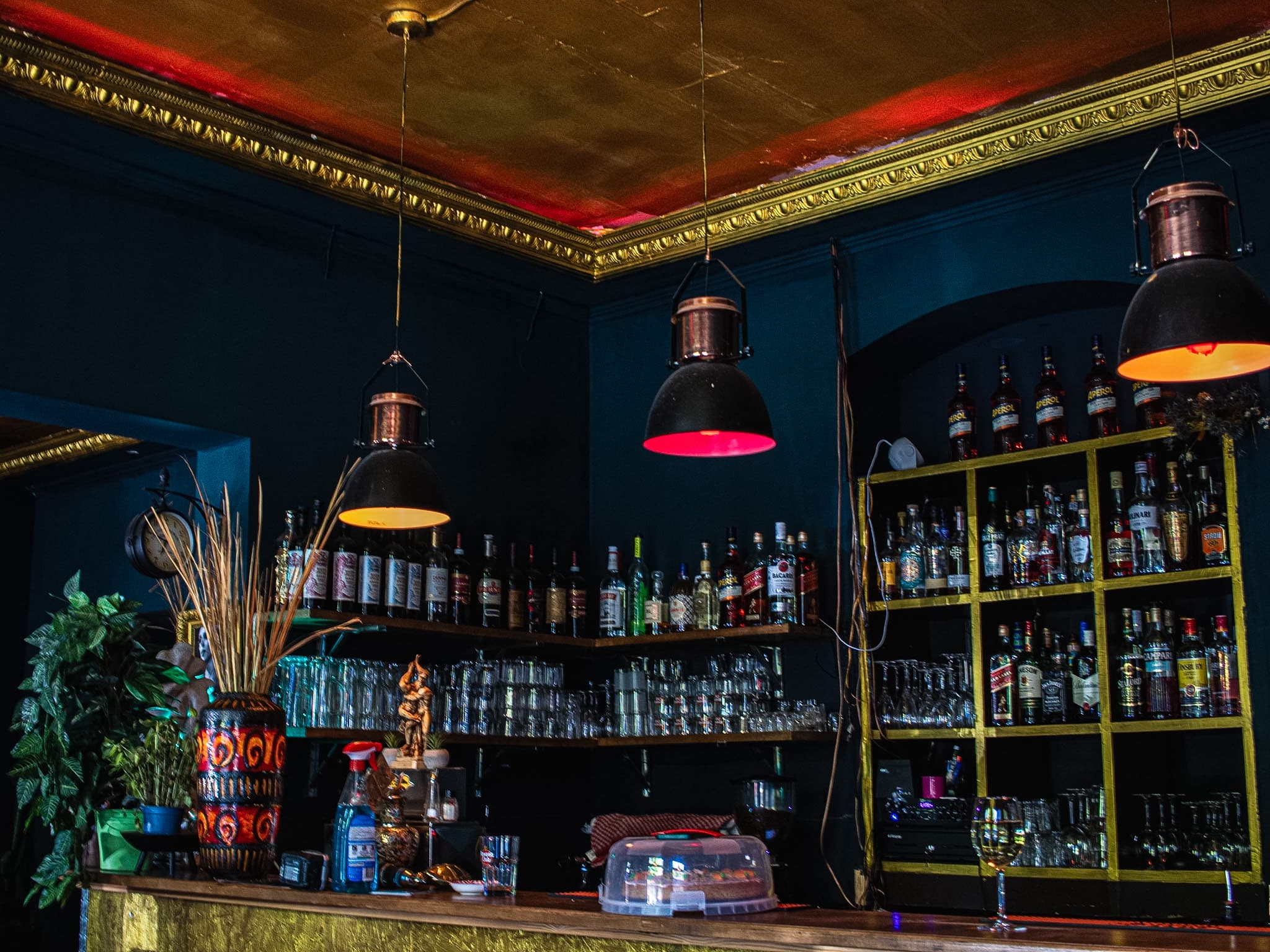 Atmospheric bar interior at Beetroot Berlin with gilded ceiling, warm amber pendant lamps, and bottle shelves